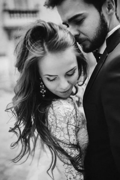 黑白照片 新婚夫妇幸福地拥抱和亲吻在古老的欧洲城镇街道 漂亮的新娘穿着白色婚纱和英俊的新郎在一起 婚礼当天 — 图库照片