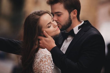 Eski Avrupa mahallesinde sarılıp öpüşen mutlu yeni evli çift, beyaz gelinlikli muhteşem gelin ve yakışıklı damat. düğün günü.