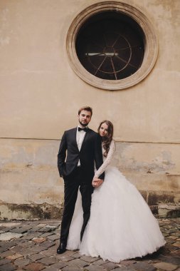 Tarz sahibi gelin ve damat Avrupa şehir caddesinde nazikçe sarılıyor. Antik binanın yakınlarında kucaklaşan muhteşem bir çift yeni evli. Romantik bir an. düğün günü.