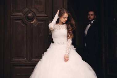 Güzel yeni evliler eski kapıyı kucaklıyor. Şık bir damadın düğün portresi ve Avrupa 'da eski bir evin yakınında genç bir gelin..