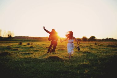 Genç ve güzel bir çift yaz günü dışarıda eğleniyor ve koşuyorlar. Gün batımında romantik bir fotoğraf. Aşk hikayesi.