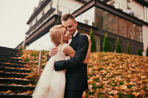 黄金の黄色の秋の公園で幸せな若い夫婦 結婚式の日に抱きしめる美しい花嫁とスタイリッシュな新郎 — ストック写真