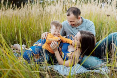 Mutlu bir aile çimlerin üzerinde eğleniyor. Aile, Meadow 'daki hayattan zevk alıyor. Anne, baba, küçük çocuk dışarıda boş vakit geçirirken gülümsüyor..