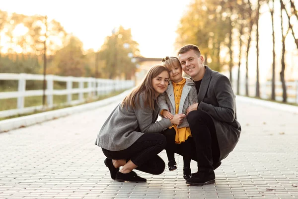 父と母は手で小さな娘を抱いていて秋の公園を歩いていて幸せな家族は屋外で楽しんでいます お父さんとお母さんと赤ちゃんの日 — ストック写真