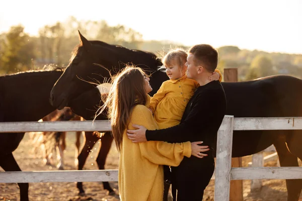 在秋天的公园里 年轻的父母和小女儿在马旁边散步 爸爸和妈妈抱着女婴 快乐的家庭观念 — 图库照片