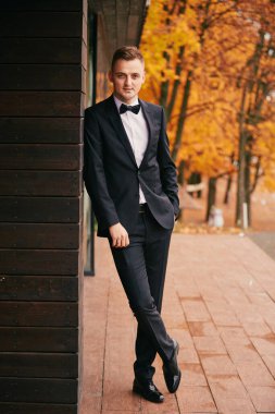 Sonbahar parkında düğün günü siyah takım elbiseli şık genç damat..