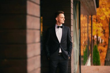 Sonbahar parkında düğün günü siyah takım elbiseli şık genç damat..