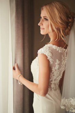 Güzel gelin pencerenin yanında duruyor ve gülümsüyor. Düğün Günü.