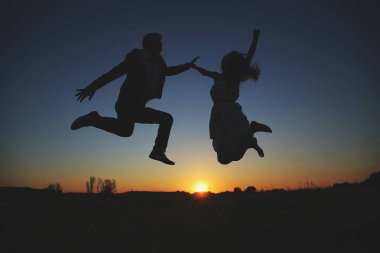 Genç çiftin silueti atlıyor ve yaz akşamları dışarıda eğleniyor. Gün batımında romantik bir fotoğraf. Aşk hikayesi