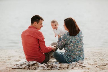 Suyun kenarında oturan mutlu bir aile. Anne, baba ve küçük kızları birlikte oturuyorlar. Dışarıda mutlu bir aile. Gülümseyen insanlar