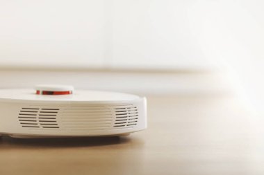 Beyaz robotik süpürge, oturma odasının iç tarafındaki plastik zeminde toz temizliyor. Akıllı elektronik temizlik teknolojisi. akıllı ev.