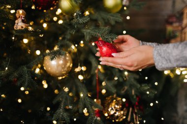 Noel topunu ağaca bokeh ışıklarıyla asan kadın. Noel süslemesi tutan bir kadının ellerinin yakın plan fotoğrafı, Noel ağacına asılı bir kadın oyuncağı. Noel 'i el dekorasyonu