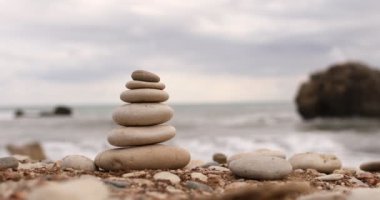 Mavi deniz arka planında güneşli bir günde deniz kıyısındaki piramit taşları. Kızın eli piramidi yok ediyor. İyi tatiller. Çakıl taşı plajı, sakin deniz, seyahat yeri. seçici odak.