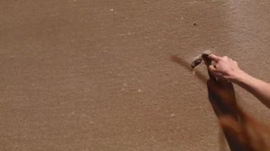 El yazısıyla yazılmış, altın kumda çizilmiş bir kalp. Sahilde, denizde ya da okyanusta bir dalga tarafından sürüklenmiş. Sevgililer Günü tatili, kırık kalp suyla yıkanır gider. seçici odak.