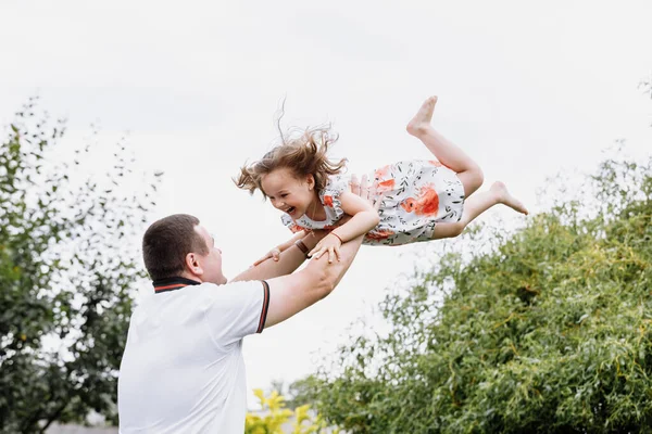 Young father throwing his baby daughter high in the sky in the park in summer day. fathers day — Stock Photo, Image