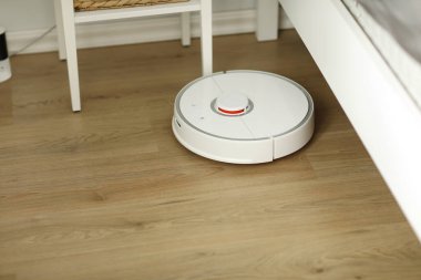 Beyaz robotik süpürge, oturma odasının iç tarafındaki plastik zeminde toz temizliyor. Akıllı elektronik temizlik teknolojisi. akıllı ev.