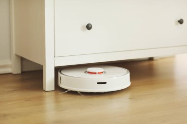 Beyaz robotik süpürge, oturma odasının iç tarafındaki plastik zeminde toz temizliyor. Akıllı elektronik temizlik teknolojisi. akıllı ev.