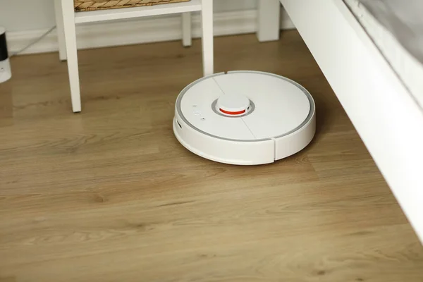 White robotic vacuum cleaner on laminate floor cleaning dust in living room interior. Smart electronic housekeeping technology. smart home.