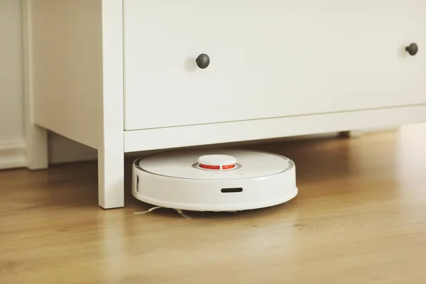 White robotic vacuum cleaner on laminate floor cleaning dust in living room interior. Smart electronic housekeeping technology. smart home.