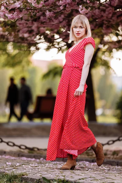 春天城市里穿着红色连衣裙的金发美女很时髦 穿着红色衣服的漂亮女孩在城市街道上摆姿势 在城市里散步的女人 — 图库照片