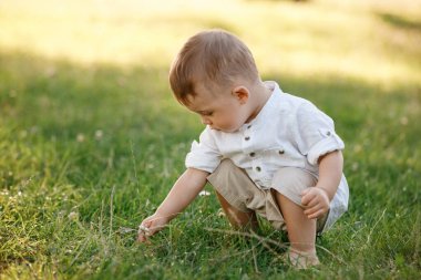 Yaz günü parkta çimlerin üzerinde oturan sevimli erkek bebek. Moda ve şirin elbiseli çocuk..