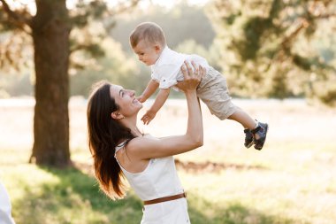 Anne, yaz tatilinde oğlunu kusar ve doğada döndürür. Anne ve kız parkta oynuyorlar. Çocuk uçuyor. Arkadaş canlısı aile kavramı. - Yakın çekim. seçici odak
