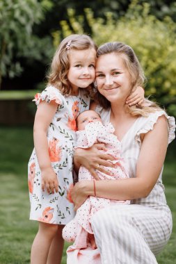 Sevgi dolu bir anne ve iki sevimli çocuğun portresi. Küçük bir kız ve yeni doğmuş bir kız bebek ve annesi yaz günü dışarıdalar. Mutlu aile parkta birlikte vakit geçirirdi..