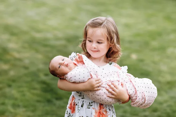 Linda niña sosteniendo a su hermana recién nacida más joven al aire libre. Relaciones entre parientes. Dos hermanas se aman. estilo de vida familiar —  Fotos de Stock