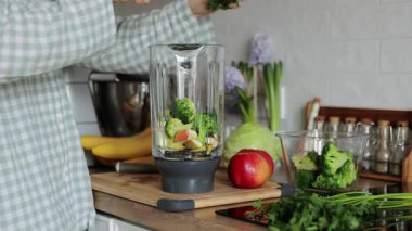 Bilinmeyen kadın evde sağlıklı bir detoks kahvaltısı hazırlıyor. Kadın elleri maydanozu blender kasesine atar, taze yeşil vejetaryen meyve sebzeleri hazırlar. Temizlenmek için içecek, enerji sağlar.