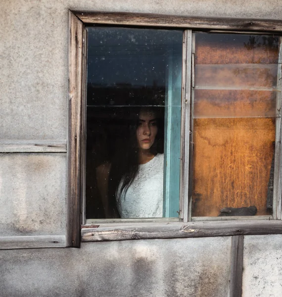 girl by the window in a wooden old abandoned house with dim light