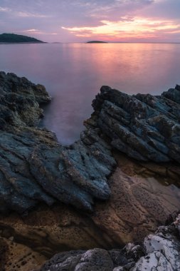 günbatımı denizde taşlarla ön planda