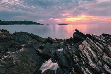 günbatımı denizde taşlarla ön planda