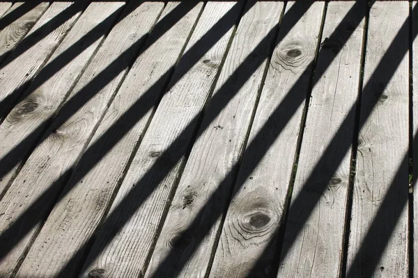 Dark diagonal shadows across weathered gray wood grain boards abstract horizontal background texture