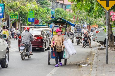 Phnom Penh, Kamboçya - 8 Nisan 2018: Birçok ağaç, mopedler, arabalar ve onun mobil satış standı ile kadın bir sokak satıcısı ile tipik Kamboçyalı sokak görünümünü