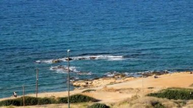 Otel penceresinden deniz manzarası, açık mavi deniz, açık esinti, kumlu plaj. Deniz kenarında iki genç yürüyüş