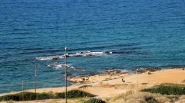 Otel penceresinden deniz manzarası, açık mavi deniz, açık esinti, kumlu plaj. Deniz kenarında iki genç yürüyüş