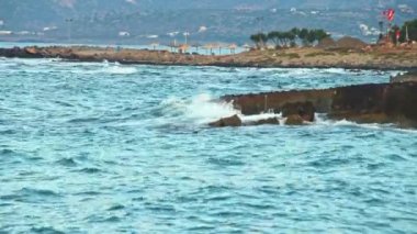 Fırtına öncesinde denizin akşam manzarası, bir sürü hareket, mavi dalgalar, beyaz köpük ve sıçramalar, bayraklar güçlü rüzgarda evrim