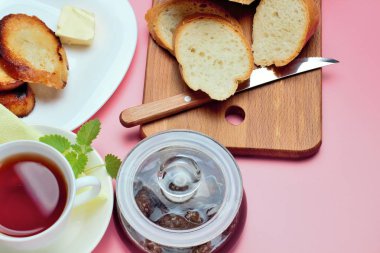 Basit bir tatlı kahvaltı için ayarlayın, tost baget, çay, tereyağı, çam kozalağı reçel. Parlak renkler, yüksek kontrast, pembe arka plan.