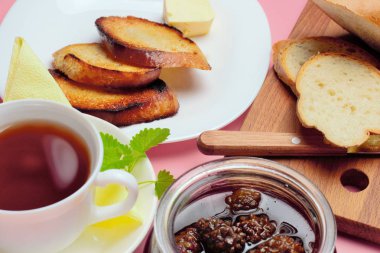 Basit bir tatlı kahvaltı için ayarlayın, kızarmış ekmek, çay, reçel, pembe bir arka plan üzerinde.