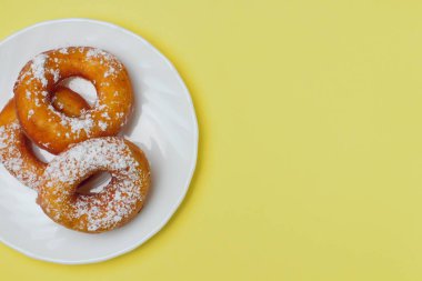 Parlak sarı bir arka plan üzerinde beyaz bir plaka üzerinde pudra şekeri ile iştah açıcı çörekler, metin için bol alan, düz yatıyordu, parlak renkler, yüksek kontrast.