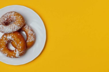 Sarı bir arka plan üzerinde beyaz bir plaka üzerinde pudra şekeri ile iştah açıcı çörekler, metin için bol alan, düz yatıyordu, parlak renkler, yüksek kontrast.