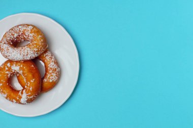 Mavi bir arka plan üzerinde beyaz bir plaka üzerinde pudra şekeri ile iştah açıcı çörekler, metin için bol alan, düz yatıyordu, parlak renkler, yüksek kontrast.