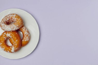 Mor bir arka plan üzerinde beyaz bir plaka üzerinde pudra şekeri ile iştah açıcı çörekler, metin için bol alan, düz yatıyordu, parlak renkler, yüksek kontrast.