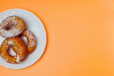 Turuncu bir arka plan üzerinde beyaz bir plaka üzerinde pudra şekeri ile iştah açıcı çörekler, metin için bol alan, düz yatıyordu, parlak renkler, yüksek kontrast.