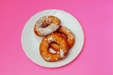 Pembe bir arka plan üzerinde beyaz bir plaka üzerinde pudra şekeri ile iştah açıcı çörekler, metin için bol alan, düz yatıyordu, parlak renkler, yüksek kontrast.