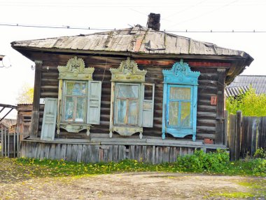 Pencereleri ve oyulmuş bantları olan eski bir kütük ev, eğimli bir bina. Parlak doğal renkler, yüksek kontrast.