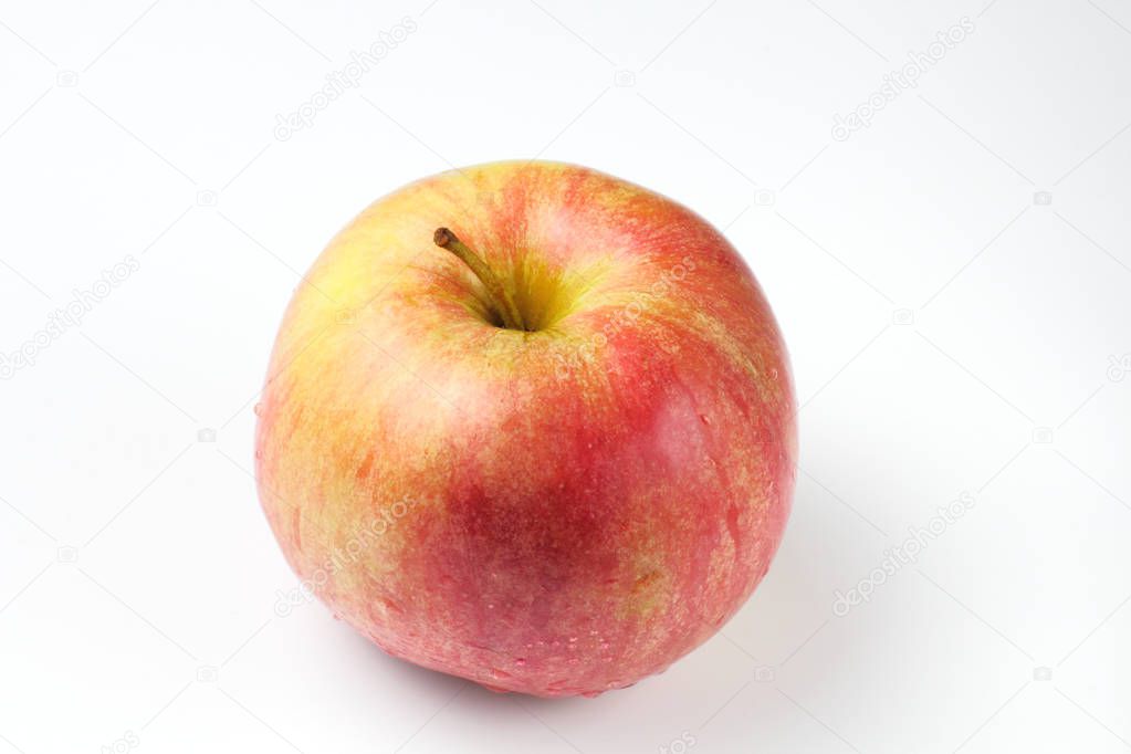 Fresh bright yellow-red apple with small droplets of water on a white background, high contrast.