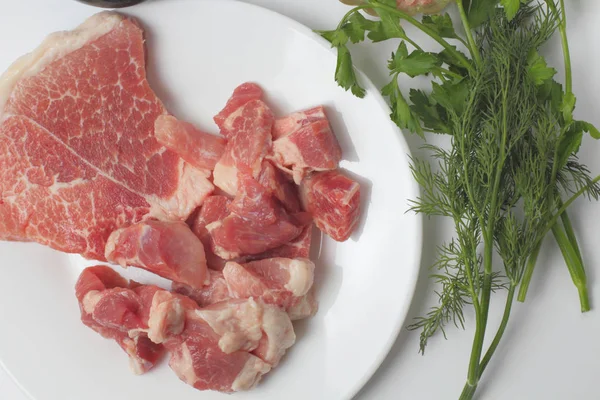 Fresh pork is cut into portions on a large plate, spicy herbs, white background, bright natural colors, top view.