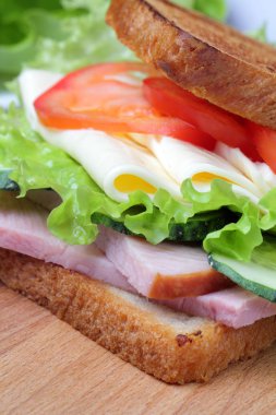 Jambonlu sandviç, marul, peynir dilimleri, domates, kesme tahtası, parlak doğal renkler.