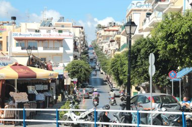 Agios Nikolaos, Girit, Yunanistan, 10/14/2015 Resimli Editoryal Motosikletler, scooterlar ve arabalar, restoran ve kafe masalarının etrafında, önde gelen dar bir şehir caddesinde.